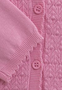 Różowy sweter z dzianiny z teksturowanym wzorem, ściągaczami na mankietach i dwoma różowymi guzikami z przodu. Miękki materiał o gładkim wykończeniu.