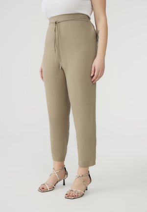 Pantaloni khaki con vita a cordoncino, taglio affusolato e texture liscia, abbinati a sandali con tacco a strappo.