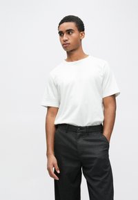 Balta, īsrokās T-krekls kopā ar teksturētām tumši pelēkām biksēm. T-krekls ir brīva piegriezuma ar apaļu apkakli, piedāvājot ikdienišķu izskatu.