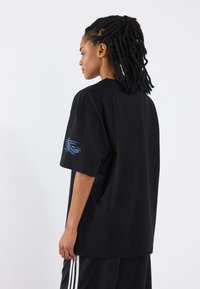 Black cotton t-shirt with a relaxed fit, featuring a blue graphic design on the left sleeve. The fabric appears smooth with a classic crew neck.