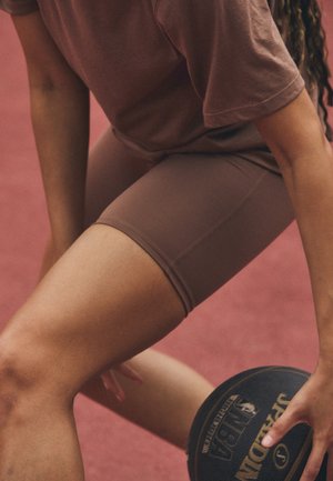 Person in brown sportswear dribbling a black Spalding basketball on a red court surface.