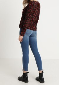 Haut noir à manches longues avec motif floral rouge, associé à un jean bleu ajusté avec des ourlets fendus et des bottines noires.
