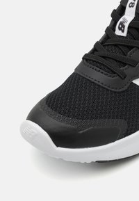 Baskets de sport noires avec une tige en mesh, des accents en synthétique texturé, un embout lisse et une semelle en caoutchouc blanche. Les lacets sont noirs avec des détails de logo.