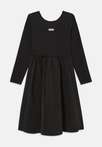 Must hõlmik, millel on pehmest materjalist sobituv pikkade varrukatega pluus ja kulgeva lõikega seelik, millel on kokku kogumise detail. Rinnas Calvin Kleini logo patsch.