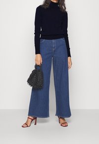 Laivastonsininen pooloneulepaita, leveälahkeiset siniset farkut, musta verkkomallinen käsilaukku ja tummanpunaiset remmikkäsandaalit korkealla korolla.