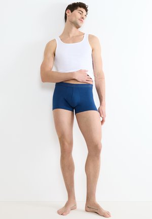 Boxer shorts in cotone blu con una vestibilità aderente e una vita caratterizzata da un branding discreto. Indossati con una canotta bianca, evidenziando una silhouette elegante.