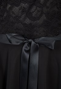 Tissu en dentelle noire à motif floral au-dessus d'un ruban en satin noir lisse noué en nœud sur un matériau transparent sombre en dessous.