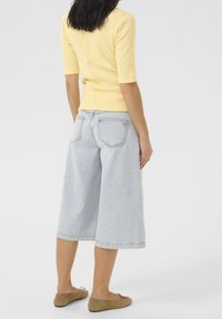 Top giallo a maniche corte abbinato a pantaloni culotte in denim larghi di colore blu chiaro e scarpe brown slip-on. L'outfit presenta uno stile aderente e un tessuto casual.