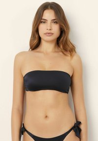 Svart bandeau-bikinitopp med slät textur och minimalistisk design. Har en strapless-stil och passar med en botten som knyts i sidorna.