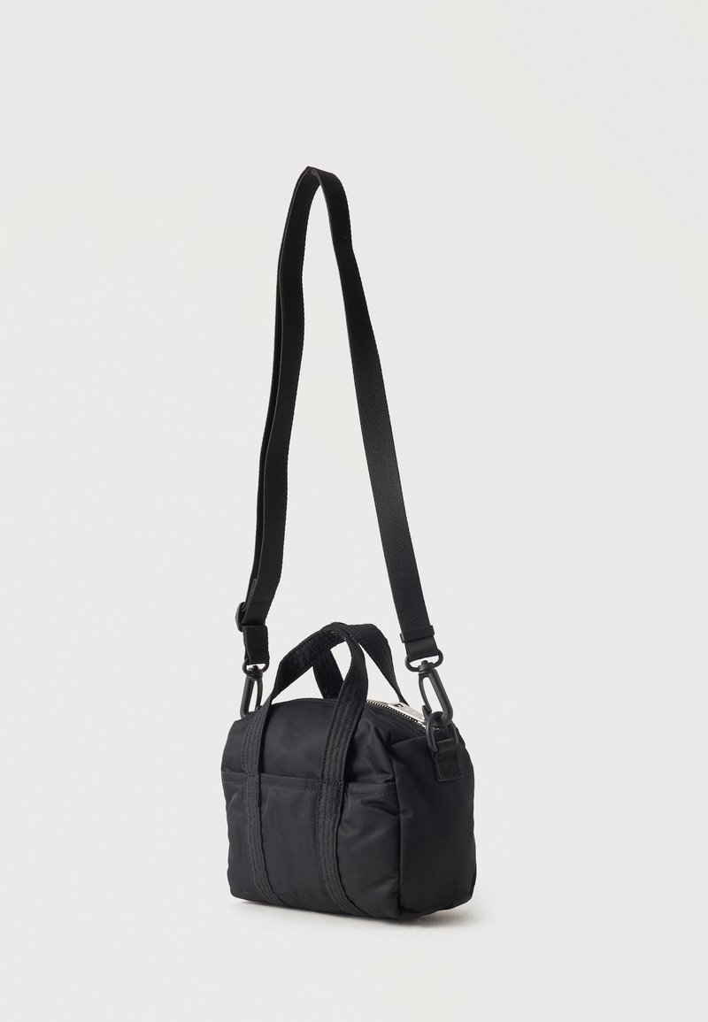 Piccola borsa a tracolla rettangolare nera con tasca frontale, manici corti e tracolla lunga regolabile su sfondo chiaro.