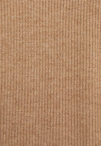 Strukturiertes Strickgewebe in einem warmen Tan-Ton, mit vertikalen Rippen für ein reichhaltiges, geschichtetes Erscheinungsbild und einem weichen, natürlichen Fasergefühl.