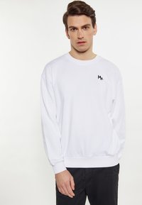 Sweatshirt alb cu guler rotund și umeri lăsați. Prezentă un mic logo negru "Mr." pe piept și manșete ribbate la mâneci și la baza.
