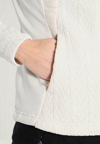 Maglione bianco con un motivo a maglia testurizzato sulle maniche, corpo liscio e una tasca laterale con dettagli in zip dorata.