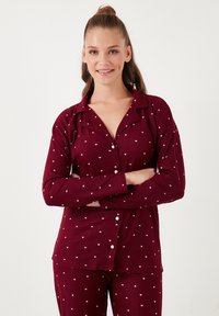 Bordo pidžama set od mekanog materijala s bijelim uzorkom srca, dugih rukava, s gumbima sprijeda, i odgovarajućim hlačama opuštenog kroja.