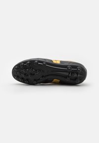 Suela de bota de fútbol negra y amarilla con tacos circulares y una superficie texturizada y duradera. Bordes reforzados visibles.