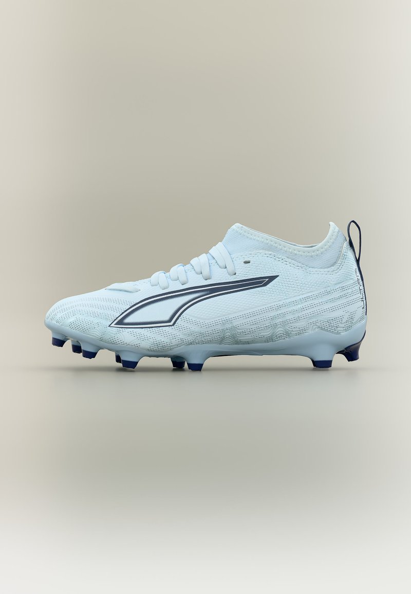 Chaussure de soccer blanche avec logo noir, dessus texturé, lacets et crampons noirs sur la semelle, présentée sur un fond neutre.