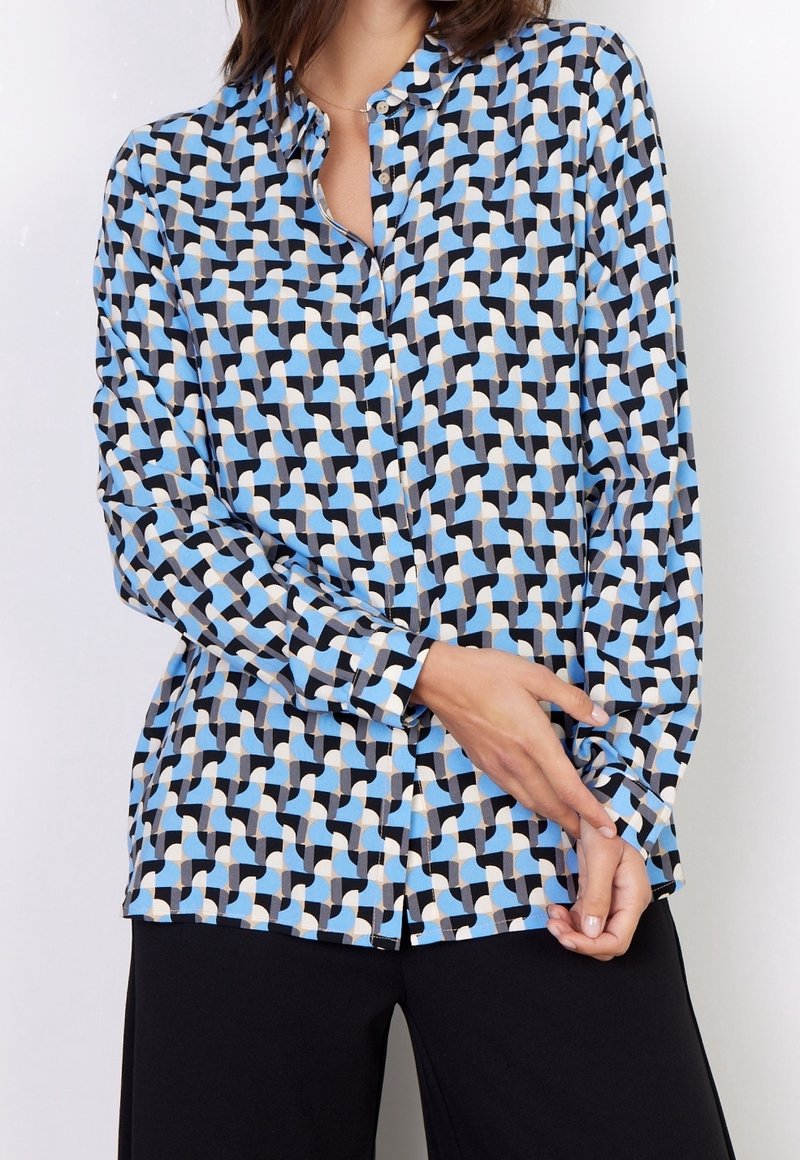 Camisa abotonada con un patrón geométrico en azul claro, negro y crema, con mangas largas y corte recto. Textura de tela suave.