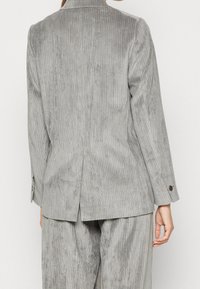 Blazer in corduroy grigio con un motivo a coste testurizzato, spacchetto posteriore singolo e polsini con bottone. Vestibilità su misura, progettato con maniche dritte.