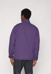 Lila Jacke mit hohem Kragen, elastischen Bündchen und entspanntem Schnitt. Hergestellt aus strukturiertem Material, mit glatter Oberfläche und minimaler Detailgestaltung.