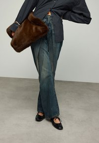 Wijd uitlopende lichtblauwe jeans gecombineerd met een donkergeruit overhemd en een donkerbruine tas van nepbont. Zwarte ballerina's maken de outfit compleet.