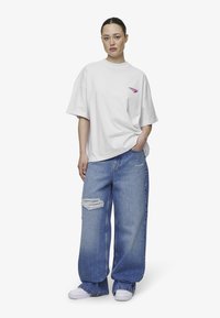 Hvit oversized t-skjorte med rosa logo, kombinert med lyseblå vide jeans med rippingdetaljer, og hvite sneakers.