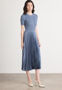 Světle modré plisované šaty s krátkými rukávy, ribbed vrchní částí a hladkým textilním materiálem. Mají siluetu A-line a končí pod koleny.