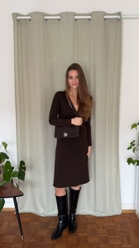 Brązowa dopasowana sukienka z długim rękawem, czarne kozaki za kolano oraz czarna torebka na ramię z okrągłą metalową klamrą, na tle jasnej zieleni.