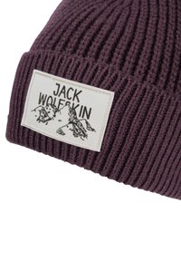 Bonnet en tricot côtelé violet fabriqué en matériau doux, avec une étiquette rectangulaire blanche portant "JACK WOLFSKIN" et des graphismes de montagnes.