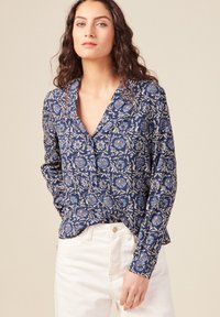 Blusa blu navy con motivo floreale in tonalità di blu e arancio. Presenta un collo a V e maniche lunghe, realizzata in tessuto leggero.