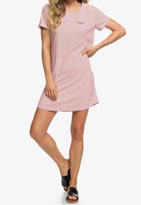 Robe mini rayée rouge et blanche avec manches courtes et col rond. Présente un petit logo rouge sur la poitrine. Portée avec des sandales noires à enfiler.