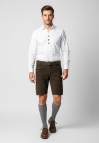 Weißes Hemd mit floralem Stickerei, kombiniert mit braunen Shorts, grauen Kniestrümpfen und braunen Lederschuhen.