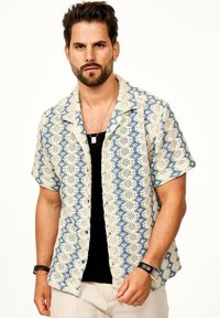 Kurzärmliges Hemd aus leichtem Stoff in Creme mit blauen wellenförmigen Mustern. Verfügt über einen lässigen Kragen und Knöpfe vorne.
