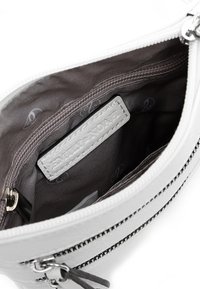 Interno di una borsa in pelle bianca con foderatura grigia, dotato di una tasca con zip e un'etichetta del marchio. Visibili dettagli in pelle testurizzata e cuciture.