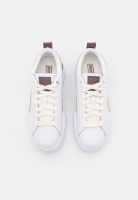 Weiße Sneakers mit glattem Lederoberteil, cremefarbenen Schnürsenkeln und kastanienbraunen Akzenten an Ferse und Seite. Abgerundete Zehenform und flache Sohlenkonstruktion.