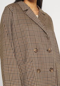 Brun och beige rutigt dubbelknäppt jacka med stora knappar, slagkrage och sidofickor. Tillverkad av texturerad tyg.