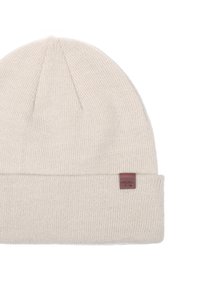Beige Strickmütze mit umgeschlagenem Bündchen und gerippter Textur. Mit einem kleinen braunen Lederetikett mit geprägt beschriftetem Text an der Seite.