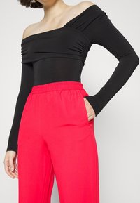 Svart off-shoulder bodysuit med rynkdetaljer, kombinerad med löst sittande, rosa byxor med elastisk midja och sidofickor.