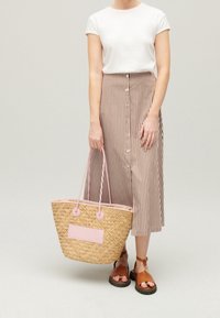 Vävd stråväska med rosa detaljer, rund form, två handtag och platt botten, kombinerad med en vit topp och en randig midikjol.