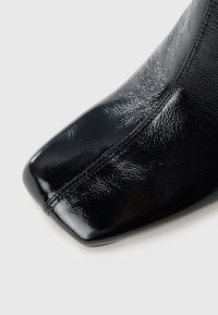 Μαύρο δερμάτινο μποτάκι αστραγάλου με γυαλιστερό φινίρισμα, τετράγωνη μύτη και διακριτή υφή. Διαθέτει κομψό σχεδιασμό με ελάχιστες ραφές.