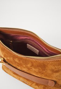 Geantă din suede de culoare maro caldă, cu o curea din piele fină. Fermuar auriu, căptușeală burgundy și un buzunar interior cu etichetă.