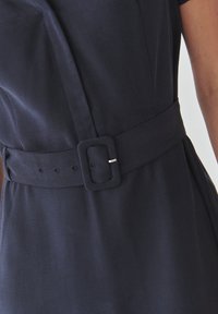 Marineblauwe jurk met een brede riem met een vierkante gesp, een gladde textuur en een getailleerde vorm, met opvallende naaddetails langs de zijkant.