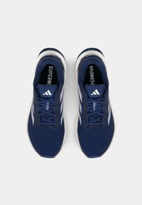 Zapatillas deportivas azul marino con parte superior de malla, acentos blancos, suela texturizada y puntera redonda. Presenta un diseño con cordones y una marca en la lengüeta.