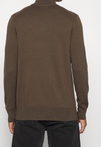 Hnědý pletený svetr s vysokým límcem, dlouhými rukávy a žebrovanými manžetami. Hladká textura a přiléhavý střih, bez viditelných vzorů či kovových doplňků.