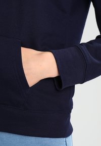 Sudadera azul marino con un bolsillo frontal y puños acanalados. Textura suave de mezcla de algodón. Primer plano de una mano en el bolsillo con un acabado liso.