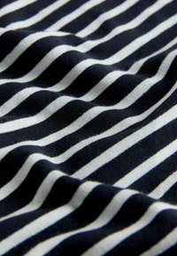 Pealtvaade pehmest kangast, millel on horisontaalsed mustad ja valged triibud, mis näitavad õrnaid voldikuid ja tekstuuri detaile.