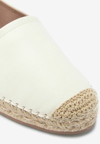 Witte leren instapschoen met een gevlochten jute punt, voorzien van zichtbare stiksels en een gladde textuur. Ontworpen voor casual gebruik.