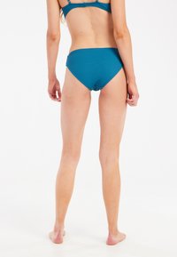 Mėlynosios bikini kelnaitės su tekstūruotu paviršiumi, aukštu liemens kirpimu ir vidutiniu dengimu. Praleistų kraštų dizainas, be siuvimo kraštų ir matomų detalių.