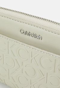 Helle Calvin Klein Geldbörse, mit geprägtem Logo-Design, glatter Textur, Hardware in Silberton und einem Reißverschluss.
