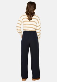 Striped sweater in cream and gold, paired with navy blue, high-waisted trousers. Relaxed fit with an elastic waistband. Brown footwear.