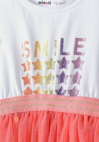 Bijela haljina s natpisom "SMILE" u duginim bojama i motivima zvjezdica. Ima koraljni tilski suknju i pojas ukrašen zlatnim detaljima.